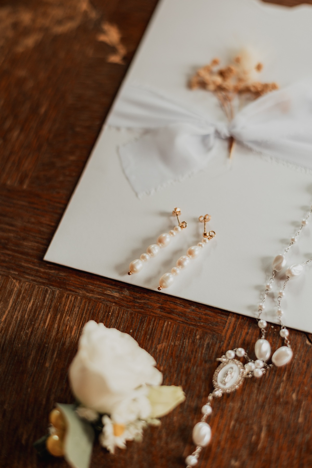 Bijoux de la mariée et faire-part posés sur une table en bois, préparatifs au Domaine Imodis