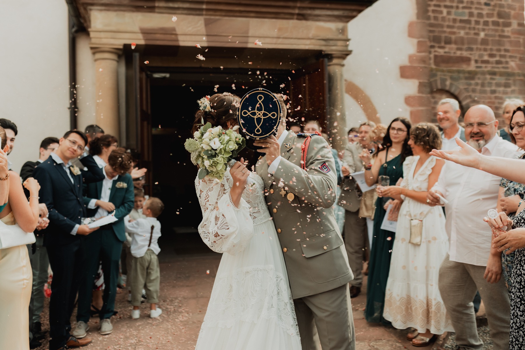 Marié protégeant la mariée des confettis avec sa casquette à la sortie de l'église à Saessolsheim en Alsace