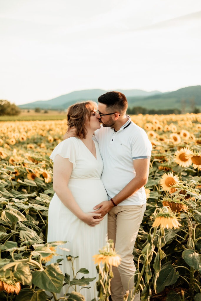 Séance photo grossesse en extérieur dans un champ de tournesols en Alsace : tendresse en couple au Bollenberg