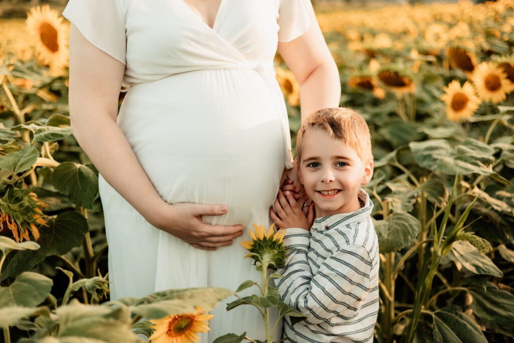 Séance maternité en extérieur en Alsace : future maman entourée de tournesols à la golden hour