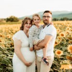 Séance maternité en famille en extérieur en Alsace : parents et grand frère dans un champ de tournesols au Bollenberg